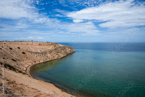 Foto Serene Coastal Cliff and Curved Bay Overlooking Calm Turquoise Ocean Under Blue