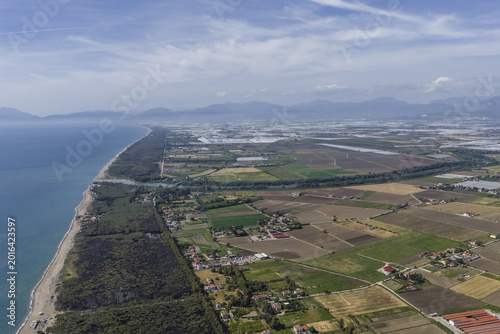 Aerial view of the Tyrrhenian coastline with sandy beaches, lush pine forests, and vast agricultural fields under a blue sky in Paestum, Campania, Italy.