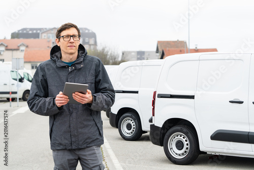 Fleet manager with digital tablet supervising rows of white delivery vans