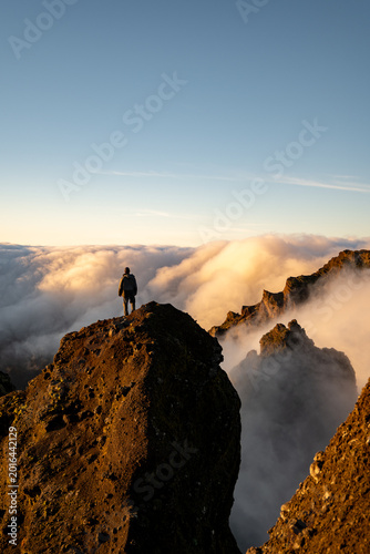 Quadro su tela lone hiker standing atop rocky mountain peak above clouds at sunrise enjoying se