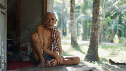 Canvas Print Elderly man resting on a wooden porch, looking at the camera, rural lifestyle