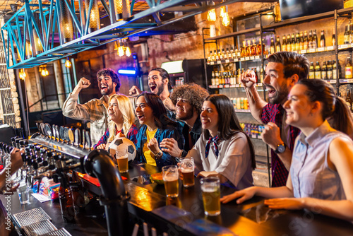 Excited fans watching football game and drinking beer in a pub.