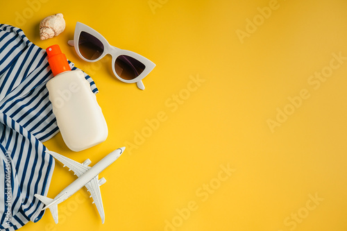 Travel, summer holiday background flat lay. Swimsuit, toy model airplane, sunglasses, sun hat and sunscreen over yellow backgrounds, copy space