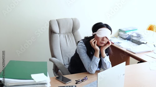 Business woman in a mask blindfolded asleep in the office. Exhausted employee in the workplace