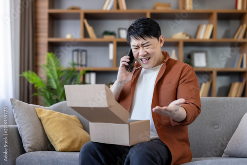 Fotografie Asian man sitting on sofa at home, opening an empty or incorrect package box and