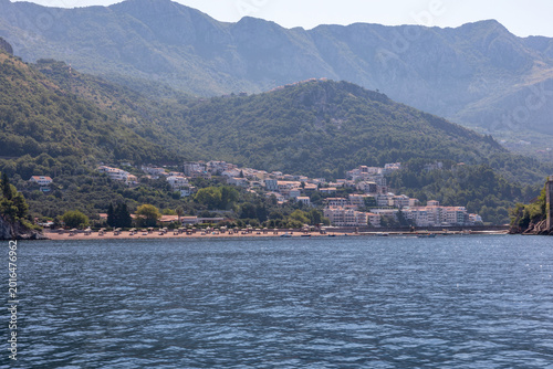 Wide view of Petrovac seaside resort with sandy beach, calm Adriatic water and green mountains in the background, Budva Municipality, Montenegro on a sunny day