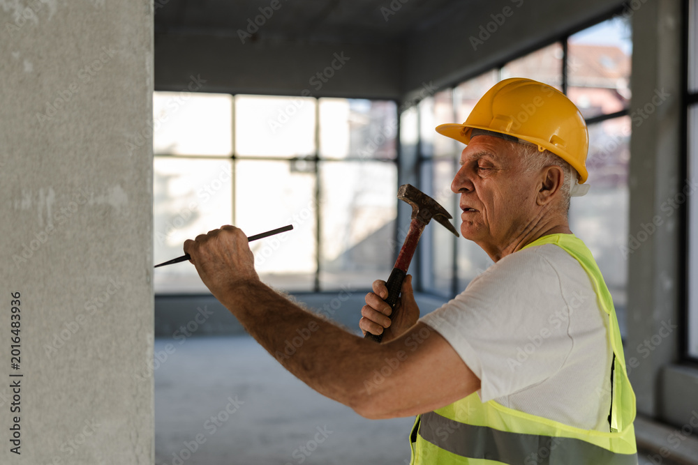 Fototapeta premium Senior Worker Builds a Wall With Hammer and Chisel in a Construction Site During Daytime