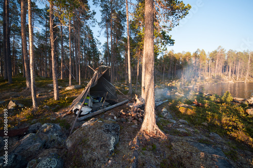 A tarp camp with a fire pit in the front in the forest wilderness of lake Inari in Lapland, Finland in summer