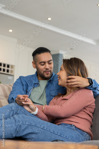 Couple sitting on sofa in modern home, holding hands, showing smartwatch, coffee table