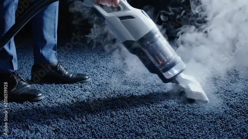 Person using a handheld steam cleaner on a dark blue carpet