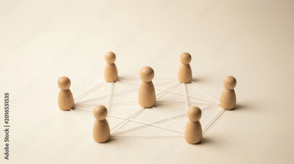 Obraz premium Wooden peg figures connected by thin lines in a network formation on a warm desk, symbolizing community, teamwork and social connection.