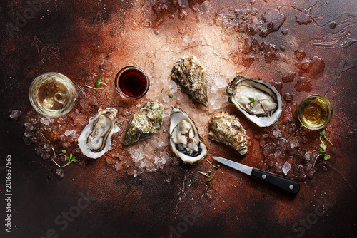 Foto Opened oysters with crushed ice, knife, micro greens, sauces and glass of wine on brown concrete background