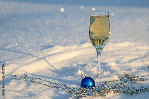 Glass of champagne stand on the white snow. New Year concept.