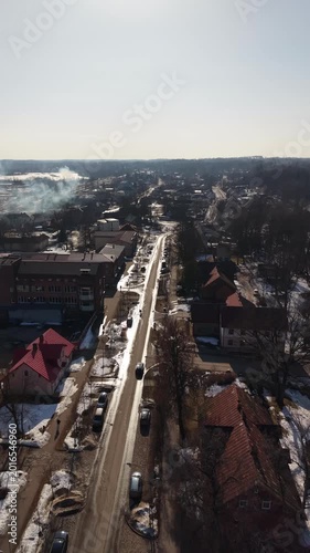 Aerial view of a snowy street in a small town with parked cars and buildings, showcasing the winter landscape and urban setting