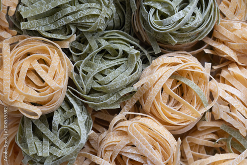 Nests of fresh egg pasta, yellow and green tagliatelle with spinach, top view.