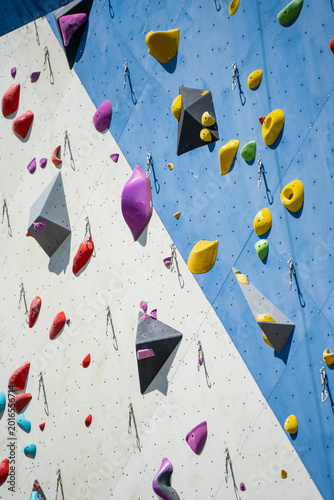 Vibrant collection of ergonomic bouldering holds and technical safety carabiners installed on a dual tone geometric climbing wall for professional athletic training and hobby