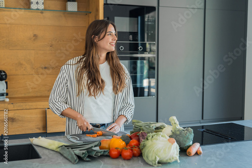 Bild auf Leinwand Woman standing in a modern kitchen, happily preparing a healthy meal by chopping
