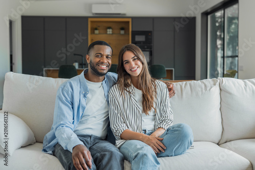 Obraz na płótnie Happy young multiracial couple relaxing and looking at the viewer from their new