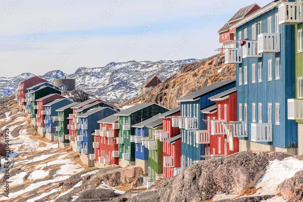 Obraz premium Dense urban housing in a Greenlandic town with colorful facades, white balconies, and snow arctic hills rising behind, Qaqortoq, Kujalleq municipality, Greenland.