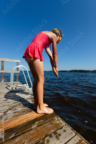 фотографія Girl stands at dock edge preparing to jump into a lake on a sunny summer day