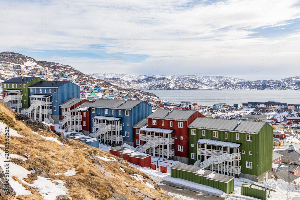 Obraz premium Colorful Inuit living houses standing on rocky hills with snow mountains and arctic fjord in the background, Qaqortoq, Kujalleq municipality, Greenland.