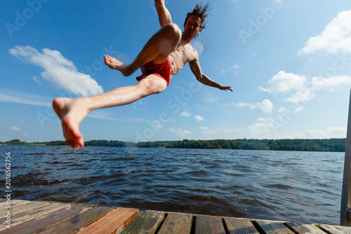 Tableau sur toile Man dives off dock with awkward fall into lake water on summer day