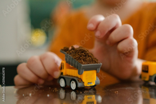 Photos Toddler child grips toy dump truck with little fingers around yellow vehicle full of dirt
