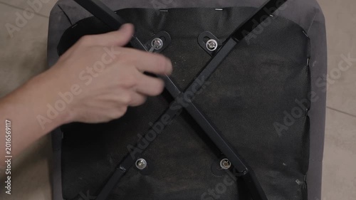 Hand untightening chair bolts, aligning metal cross supports and securing screws and washers, intimate DIY furniture assembly and maintenance scene in home workshop