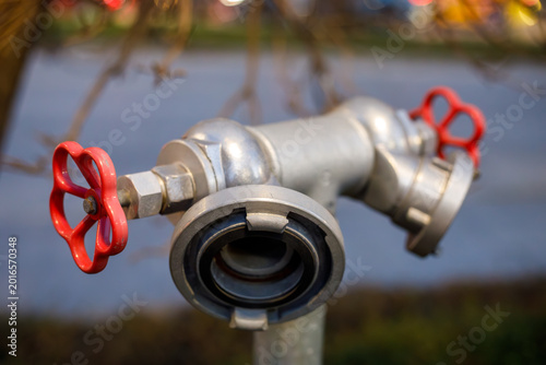 фотографія a silver metal fire hydrant standpipe with two red wheel valves and a hose coupl