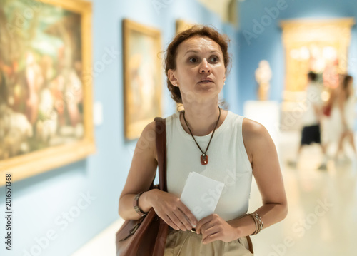 Fotografía Attractive woman holding guide book in light museum of arts and admiring works o