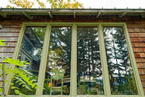 Reflections of surrounding trees in the tall windows of a cottage in the woods