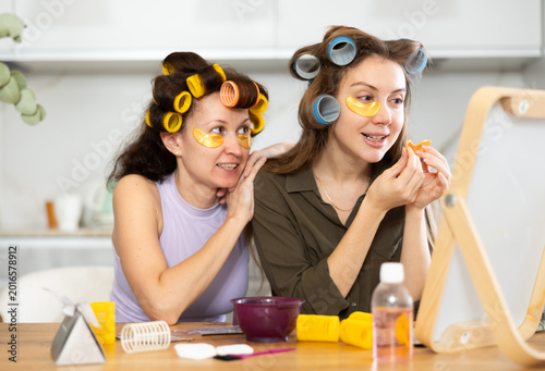 фотографія Adult and young women curl their hair with curlers and use hydrogel eye patches