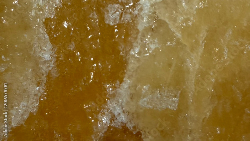 Photography Close-up texture of a warm amber-colored mineral surface with rough crystalline structure and layered formations