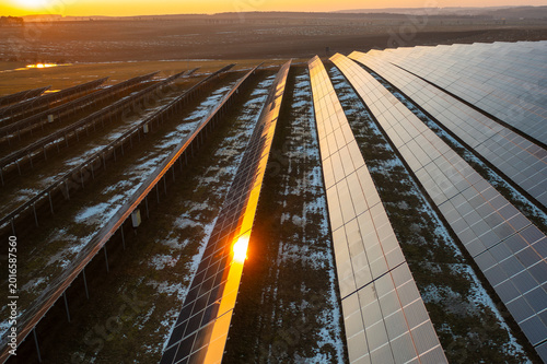 Solar panel array efficiently capturing sunlight in renewable energy field at sunset. Snow covered ground and organized rows of photovoltaic panels create a structured environment.