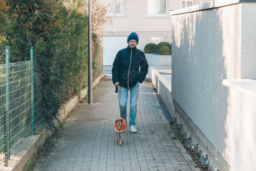 Portrait of a handsome guy walking his miniature pinscher dog on the street.