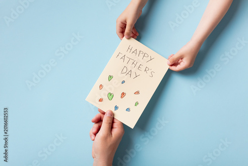 Adult and child hands holding an open handmade Father's Day card with a drawing of a family and sun.