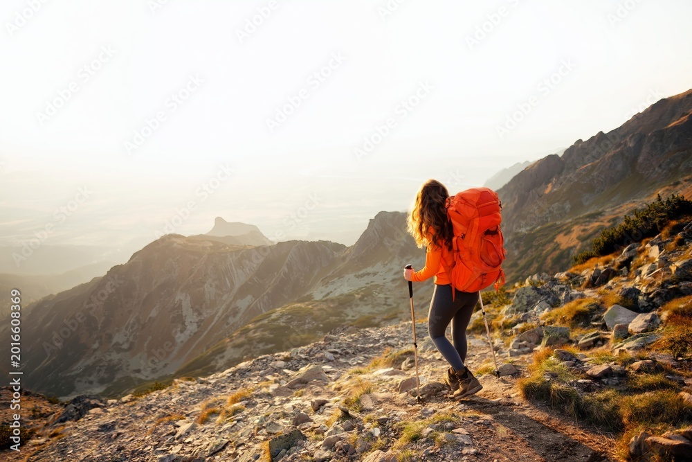 Obraz premium Orange backpack hiker walking on mountain trail background