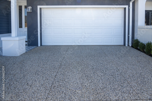 Foto A modern white sectional garage door and exposed aggregate concrete driveway of a contemporary residential home in Australia