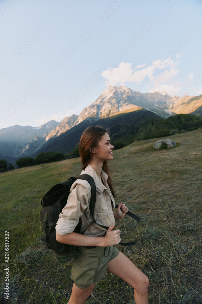 Fototapeta premium A woman hiker climbs a grassy hillside under a clear sky, with a backpack, embodying an active outdoors lifestyle and mountain exploration.