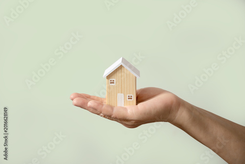 Hand holding wooden house model soft green background. Home ownership, property management, real estate insurance, homeless, foster home care