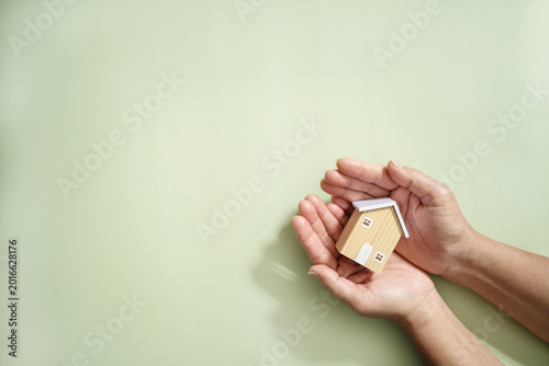 Hands hold wooden house model on light green background. Real estate, buy and sale, Property insurance, property protection, real estate safety, and residential care.
