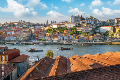 View of Porto Ribeira, Portugal, across Douro River over house rooftops, with tourist rabelo boats on the Douro River and red rooftops in the foreground