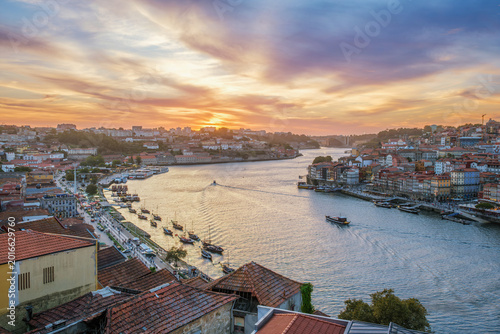 Sunset view of Douro River, Ribeira do Porto, Portugal, and Vila Nova de Gaia with a tourist boat moving past moored rabelo boats