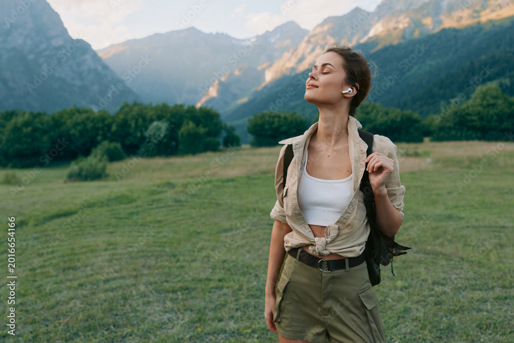 Naklejka premium A young woman in casual summer clothes enjoys a peaceful moment outdoors with mountains and green fields in the background. Concept of lifestyle and nature relaxation.