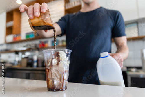 Φωτογραφία Barista pouring milk into iced coffee in modern Queensland specialty cafe