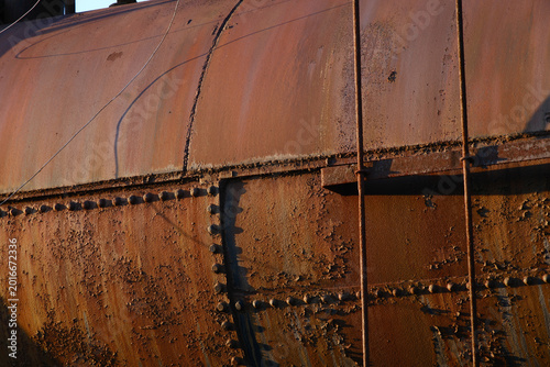 Rivets on a rusting tank with peeling paint at sunset