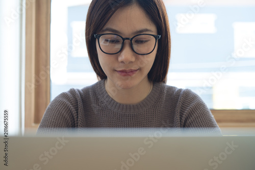 Close up of young asian woman  with eyewear concentrated working on laptop at office. Female student studying online class, searching the information, e-learning