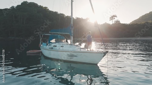 Man stands on the deck of the sailing boat and enjoys calm morning time in the secured lagoon on sunrise