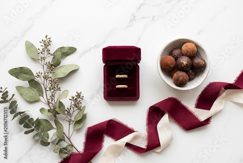 Elegant wedding rings in a burgundy velvet box with chocolate truffles and eucalyptus on a marble background