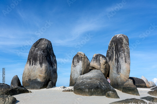 Distinctive upright granite formations known as Batu Berlayar (Sailing Rock) on Belitung Island, Indonesia, rising from white sandy beach under clear blue sky, shaped by natural weathering and coastal